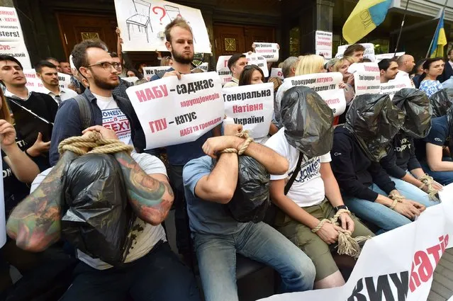 Ukrainian activists with their hands tied and plastic bags over the heads sit next to other demonstrators holding placards reading “GPO (General Prosecutors Office) is the place of tortures”, “Prosecutors torture people in Ukraine” during a protest in front of the General Prosecutors Office (GPO) in Kiev on August 17, 2016. Some hundred protesters gathered to protest against the pressure on the National Anti-Corruption Bureau (NABU) – a new body created with the purpose of cleansing government of corruption, launching of which was one of the IMF and European Comission key requirements. On August 12 NABU officials accused GPO staff of “the first open unlawful confront”, saying that two of their officers, while being on duty, were illegally detained for 11 hours. (Photo by Sergei Supinsky/AFP Photo)