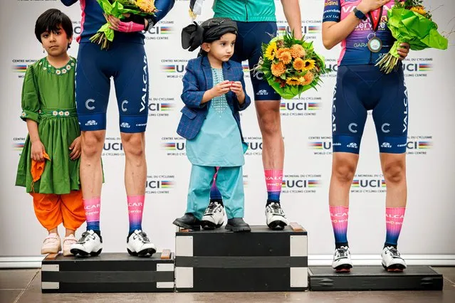 Afghan children stand on the podium with the winners of the 2022 women's road cycling championships of Afghanistan in Aigle, western Switzerland on October 23, 2022. Afghan women cyclists took part in the “Afghanistan Women's Cycling Championships” but not in Kabul as the Taliban have banned women from playing sport, barred women from many government jobs and forbidden secondary school education for girls in Afghanistan. (Photo by Valentin Flauraud/AFP Photo)