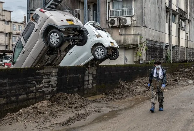 A woman walks past cars that have been swept up against a wall after torrential rain caused the nearby Kuma River to burst its banks and flood the area, on July 9, 2020 in Hitoyoshi, Japan. At least 60 people are believed to be dead and many missing after unprecedented torrential rainfall in central Japan caused 59 rivers to overflow while around 180 mudslides have occurred in 23 prefectures. (Photo by Carl Court/Getty Images)