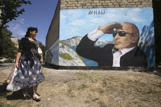 A woman walks past a graffiti depicting Russian President Vladimir Putin seen on a building in Simferopol, Crimea, August 21, 2015. The word on the graffiti reads: “Ours”. (Photo by Pavel Rebrov/Reuters)