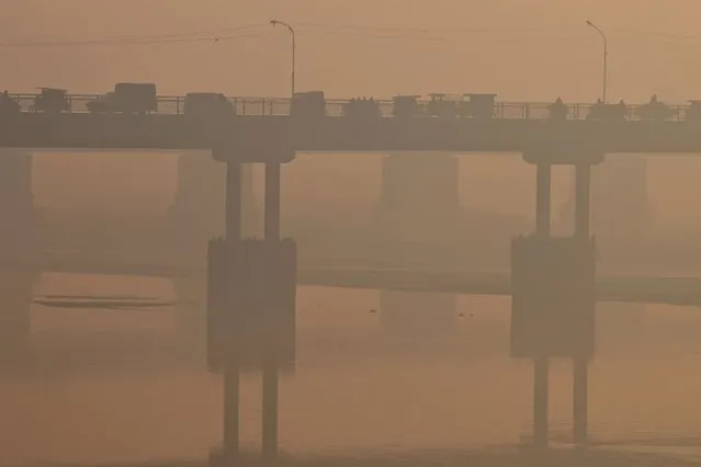 Commuters make their way across a bridge amid heavy smog in Lahore on November 22, 2022. (Photo by Arif Ali/AFP Photo)
