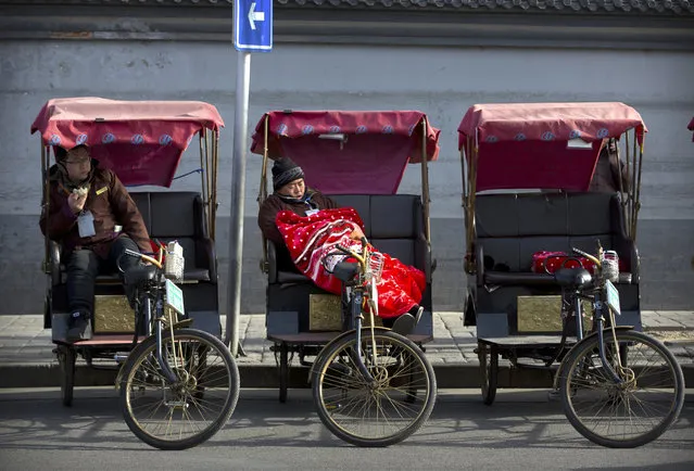 A pedicab driver rests under a blanket as he waits for tourists on a cold day in Beijing, Wednesday, January 3, 2018. Once a common sight around China's capital, rickshaws have dwindled to a small number of government-licensed drivers who operate in tourist areas. (Photo by Mark Schiefelbein/AP Photo)