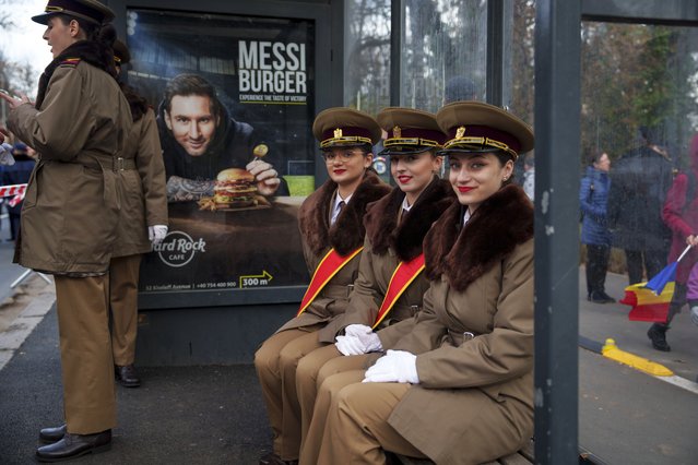 Military cadets smile while sitting in a bus stop backdropped by a billboard showing Argentinian soccer star Lionel Messi before taking part in the National Day parade in Bucharest, Romania, Friday, December 1, 2023. Tens of thousands of people turned out in Romania's capital on Friday to watch a military parade that included troops from NATO allies to mark the country's National Day. (Photo by Vadim Ghirda/AP Photo)