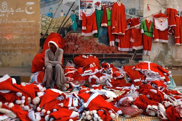 Jason, 17, waits for customers as he sells Santa Claus costumes, in front of the St. Patrick's Cathedral, on the Christmas eve celebrations, in Karachi, Pakistan on December 24, 2022. (Photo by Akhtar Soomro/Reuters)