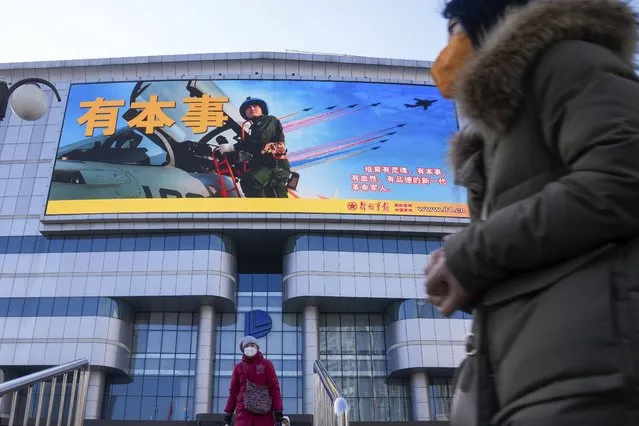 Residents wearing face masks walk by a large screen showing the Chinese People's Liberation Army Airforce outside a mall in Beijing, Monday, January 9, 2023. The Chinese military held large-scale joint combat strike drills starting Sunday, sending war planes and navy vessels toward Taiwan, both the Chinese and Taiwanese defense ministries said. (Photo by Andy Wong/AP Photo)