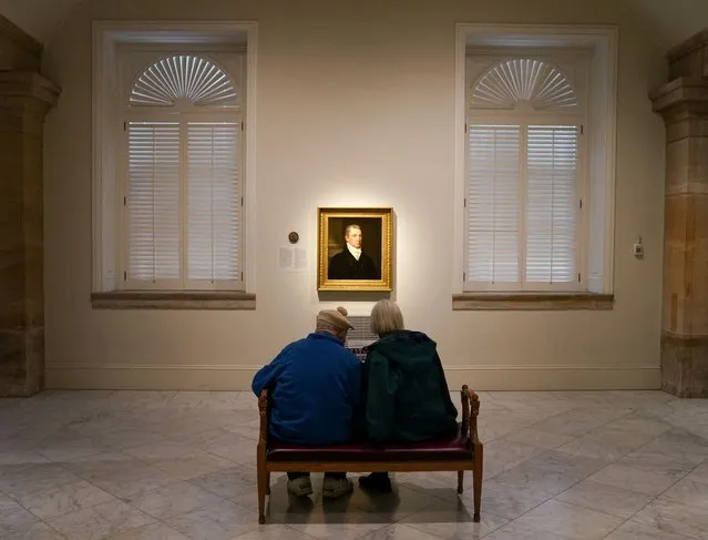 Seated in front of a portrait of President James Monroe, a couple looks at a guide to the “Americas's Presidents” exhibition at the National Portrait Gallery, a week before the Presidents' Day holiday, in Washington, U.S., February 13, 2023. (Photo by Kevin Lamarque/Reuters)