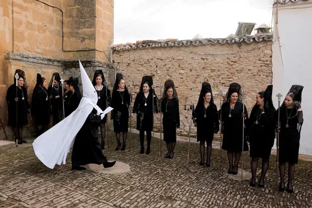 Women wearing traditional mantilla dresses and a penitent of Santo Entierro brotherhood wait outside a church before taking part in a procession during Holy Week, after processions were cancelled for the last two years due to the coronavirus disease (COVID-19) pandemic, in Ronda, Spain, April 15, 2022. (Photo by Jon Nazca/Reuters)