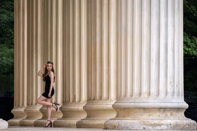 A girl poses at the entrance of the 19th century built concert hall Romanian Atheneum, a city landmark, in Bucharest, Romania, Friday, July 7, 2023. (Photo by Vadim Ghirda/AP Photo)