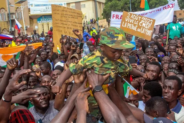 Men hold a child dressed in military uniform as they gather with thousands of anti-sanctions protestors in support of the putschist soldiers in the capital Niamey, Niger on August 3, 2023. (Photo by Mahamadou Hamidou/Reuters)