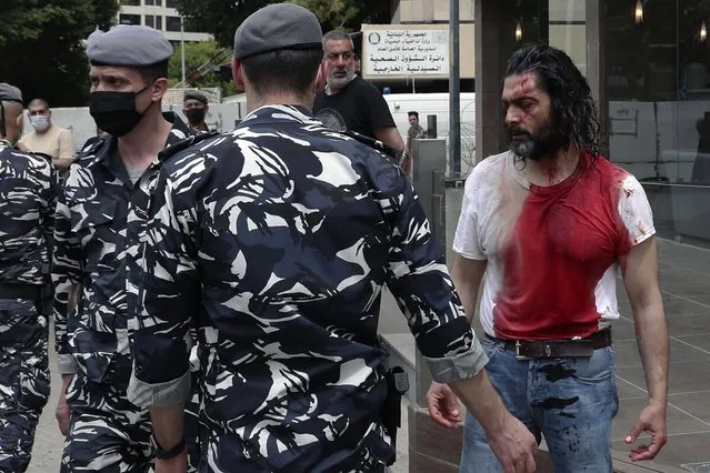 In this April 19, 2021 file photo, policemen stand guard next to a man in a blood-soaked shirt who was viciously beaten by opponents of Judge Ghada Aoun, during a sit-in outside the Justice Palace in Beirut, Lebanon. A public feud in recent weeks among prosecutors has starkly demonstrated how Lebanon's system of sectarian factions is paralyzing Lebanon's judicial system and snarling attempts to root out corruption. Aoun, a prominent prosecutor says she is trying to go after rampant corruption but her critics say she is only targeting enemies of her ally, the president. (Photo by Bilal Hussein/AP Photo/File)