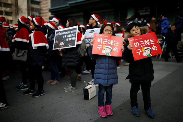 Children pose for photographs next to people dressed in Santa's costumes during a protest demanding South Korean President Park Geun-hye's resignation in Seoul, South Korea, December 24, 2016. The signs read “Arrest Park Geun-hye”. (Photo by Kim Hong-Ji/Reuters)