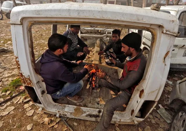 People warm themselves by a fire inside a dismantled vehicle at a scrapyard on a cold day in Srinagar December 19, 2016. (Photo by Danish Ismail/Reuters)