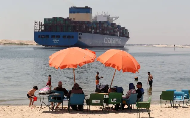 Egyptians swim in the Suez Canal as a container ship moves through it, in Ismaila, Egypt, 27 May 2021. The Suez Canal Authority (SCA) chairman Osama Rabie, in an interview with EFE News Agency in Ismailia on the eve of the start of the compensation trial against the 'Ever Given' said that the black box indicated a serious fault of the captain because the center of the ship wasn't in the middle of the entrance and entered with a high speed that is not allowed in narrow sea lanes, which led to the accident that choked the canal and entered the ship 12 meters in the deep of the shore because of the high speed. Rabie also said that “We are making a new 10 kilometers track to increase the number of passing ships and reduce the crossing time. And we're going to widen the canal 40 meters and increase the depth from 66 to 72 feet in the southern section” to prevent future accidents. (Photo by Khaled Elfiqi/EPA/EFE)