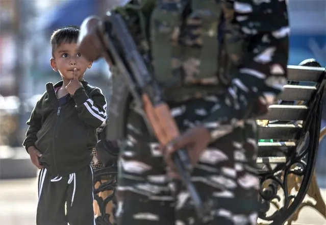 A Kashmiri child watches an Indian paramilitary soldier standing guard in Srinagar, Indian controlled Kashmir, Tuesday, August 24, 2021. Indian government forces killed two senior rebel commanders and three other militants in two separate counterinsurgency operations in disputed Kashmir, police said Tuesday. (Photo by Mukhtar Khan/AP Photo)