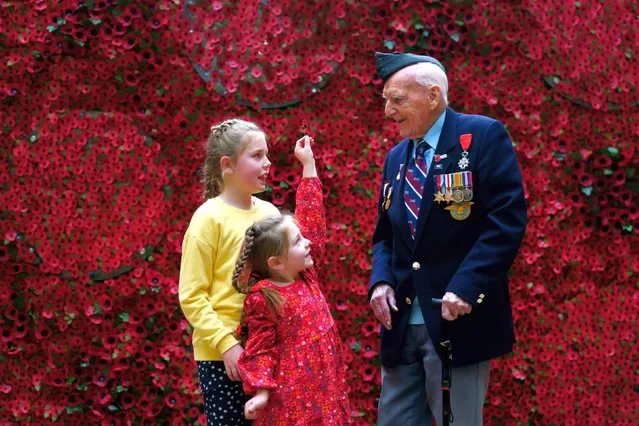 98-year-old D-Day Veteran Bernard Morgan, whose story is among those featured on the giant poppy wall, is given a poppy by Daisy and Maya Renard during the launch of The Royal British Legion 2022 Poppy Appeal, at Hay's Galleria in central London on Thursday, October 27, 2022. Members of the public will be invited to take a paper poppy from the wall and uncover the stories of members of the Armed Forces community who have received help from the Royal British Legion. (Photo by Victoria Jones/PA Images via Getty Images)