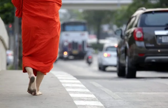 A Buddhist monk, barefoot and clothed in traditional orange-colored robes, walks alongside a road carrying busy vehicle traffic, as commuters seated in cars and buses pass, in Bangkok, Thailand, 24 February 2016. Energy friendly and non-polluting transport options remain a problem for Bangkok, public buses in the capital spew toxic black smoke and car consumption is soaring as middle class expendable incomes increase. (Photo by Barbara Walton/EPA)