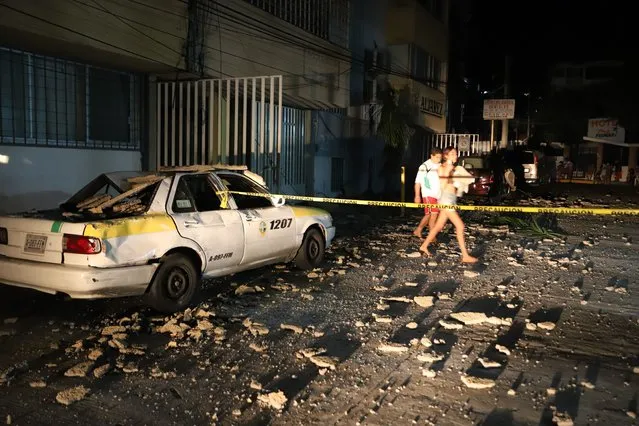 A couple walks past a taxi cab that was damaged by falling debris after a strong earthquake in Acapulco, Mexico, Tuesday, September 7, 2021. The quake struck southern Mexico near the resort of Acapulco, causing buildings to rock and sway in Mexico City nearly 200 miles away. (Photo by Bernardino Hernandez/AP Photo)