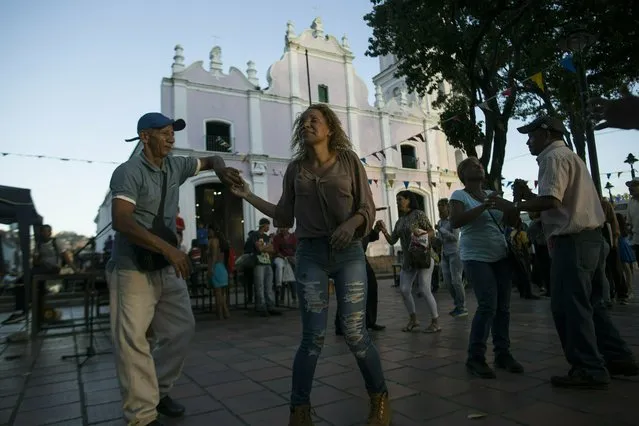 In this February 8, 2019 photo, supporters of President Nicolas Maduro dance outside the Dulce Nombre de Jesus church as Monsignor Hector Lunar performs Mass, in the Petare slum of Caracas, Venezuela. The Maduro supporters came to the plaza for 19 consecutive days in late January and early February. They set up a stage with speakers just steps from the church’s front doors, blasting loud music and politically charged speeches aimed at Lunar. (Photo by Rodrigo Abd/AP Photo)