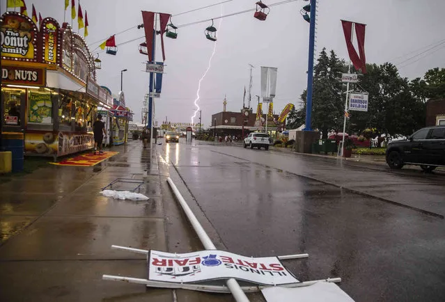 Lighting strikes in the background as a pole that was snapped at its base lies along Main Street as a storm hits the Illinois State Fair at the Illinois State Fairgrounds in Springfield, Ill., Thursday, August 12, 2021. (Photo by Justin L. Fowler/The State Journal-Register via AP Photo)