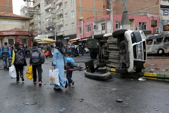 Residents walk by a vehicle, which was damaged during the clashes between security forces and Kurdish militants, as they flee after clashes between security forces and Kurdish militants from Baglar district, which is partially under curfew, in the Kurdish-dominated southeastern city of Diyarbakir, Turkey March 15, 2016. (Photo by Sertac Kayar/Reuters)