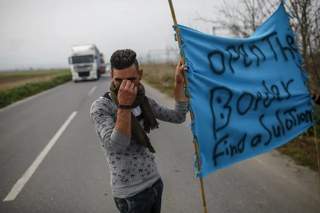 A migrant holds a banner as he blocks the road during a protest near the Greek-Macedonian border, near the town of Polykastro, Greece, April 2, 2016. (Photo by Marko Djurica/Reuters)