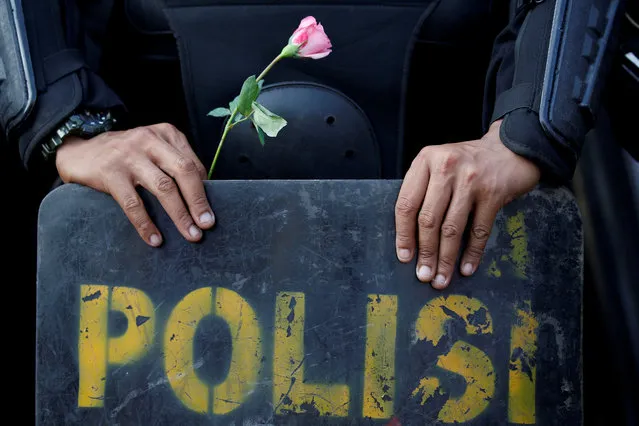 A mobile police brigade (Brimob) officer holds a flower as he stands guard on a baricade during a protest following the announcement of the last month's presidential election results outside Election Supervisory Board (Bawaslu) headquarters in Jakarta, Indonesia, May 21, 2019. (Photo by Willy Kurniawan/Reuters)