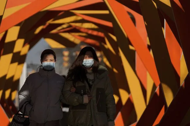 Women wearing face masks to help protect from the coronavirus walk by an art installation depicting a prosperity chamber on display outside a mall in Beijing, Monday, December 27, 2021. (Photo by Andy Wong/AP Photo)