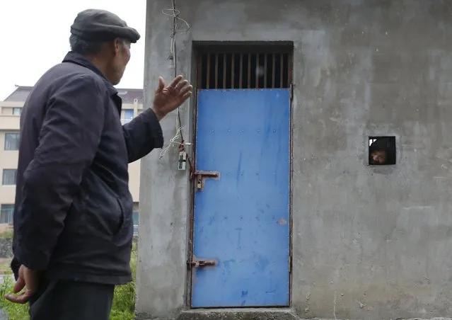 Ma Pinglin, 37, looks out as he speaks to his father through a hole on the wall of a locked house, serving as Ma's dwelling, in Houtang village, Zhejiang province, China, May 14, 2015. According to the family, Ma turned violent and often hit people and set fire in the house after he was diagnosed of mental dissociation in 2009. Ma's father had to build a small house, which cost about 20,000 yuan (3,222 USD), to lock him up, as the family cannot afford a full treatment. (Photo by William Hong/Reuters)