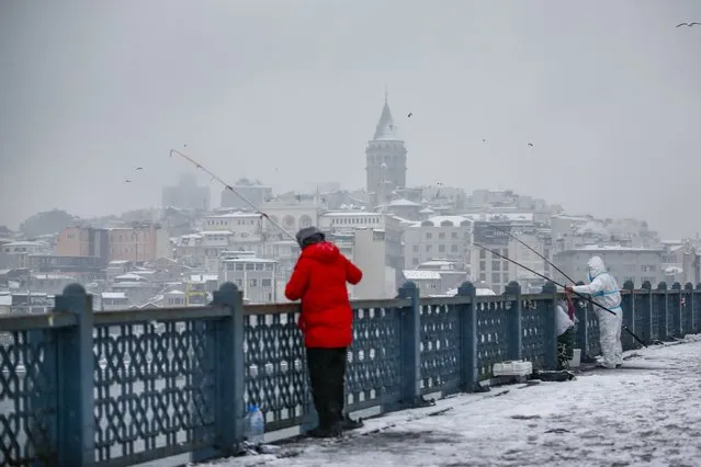 People fish in the snow on Galata Bridge over Golden Horn at Istanbul, Monday, January 24, 2022. Snow blanketed most of Turkey's largest city Monday. Flurries are forecast to continue over the next few days in Istanbul, a metropolis of some 16 million spanning two continents and bridging Europe to Asia. (Photo by Emrah Gurel/AP Photo)