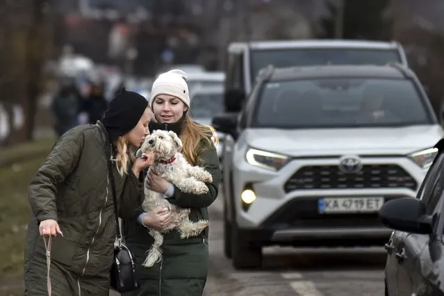 Two women walk their dogs past a queue of cars heading to the Poland border near Shehyni, western Ukraine, Tuesday, March 1, 2022. Russian shelling pounded civilian targets in Ukraine's second-largest city again, and a 40-mile convoy of tanks and other vehicles threatened the capital. Ukraine's embattled president said the tactics were designed to force him into concessions in Europe's largest ground war in generations. (Photo by Pavlo Palamarchuk/AP Photo)