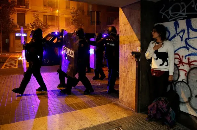 A woman takes cover as police officers walk past during a protest after a verdict in a trial over a banned Catalonia's independence referendum, in Barcelona, Spain, October 16, 2019. (Photo by Rafael Marchante/Reuters)