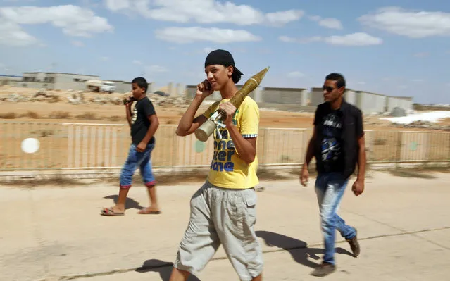A youth, with a rocket-propelled grenade (RPG) shell, uses his mobile phone as he walks out of the Rafalla al-Sihati brigade base, part of the Libyan army, after it was attacked by demonstrators in Benghazi city September 22, 2012. (Photo by Asmaa Waguih/Reuters)