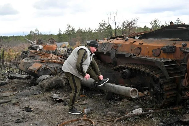 A man ties his show lace placing his foot on the barrel of a destroyed Russian tank in the vilage of Andriivka, in the Kyiv region on April 17, 2022. (Photo by Sergei Supinsky/AFP Photo)