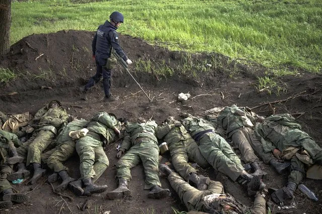 A member of Ukraine demining team checks for explosives around the bodies of 11 Russian soldiers in the village of Vilkhivka, recently retaken by Ukraininan forces near Kharkiv, Ukraine, Monday, May 9, 2022. (Photo by Felipe Dana/AP Photo)