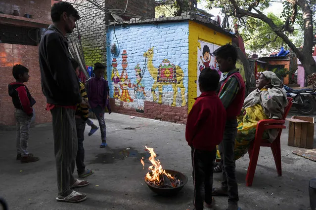 Local residents warm up around a bonfire near homes adorned with murals painted by artists from “Delhi Street Art” group at the Raghubir Nagar slum in New Delhi on December 2, 2019. (Photo by Sajjad Hussain/AFP Photo)