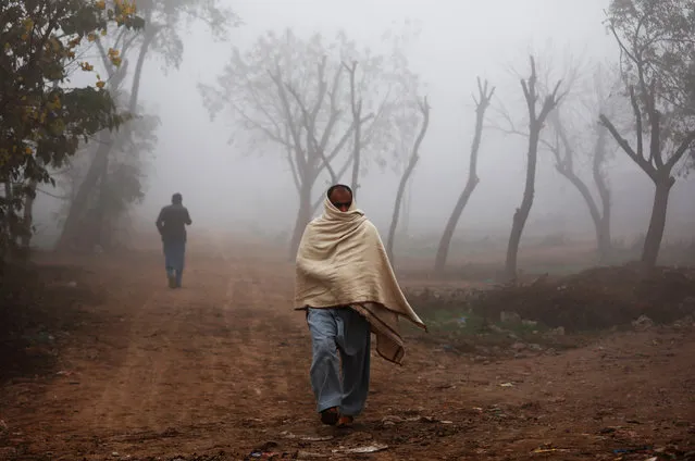 A man covers himself with a shawl as a protection from the cold weather as he walks amid dense fog in Peshawar, Pakistan on December 30, 2019. (Photo by Fayaz Aziz/Reuters)