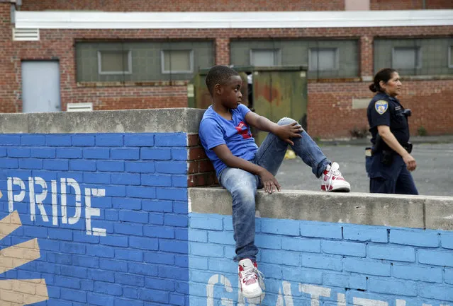 A boy sits on a wall as a member of the Baltimore Police Department walks by in the Penn North neighborhood of Baltimore, Thursday, June 23, 2016, near the site of unrest following the funeral of Freddie Gray. Officer Caesar Goodson, one of six Baltimore city police officers charged in connection to the death of Gray, was acquitted of all charges in his trial Thursday. (Photo by Patrick Semansky/AP Photo)