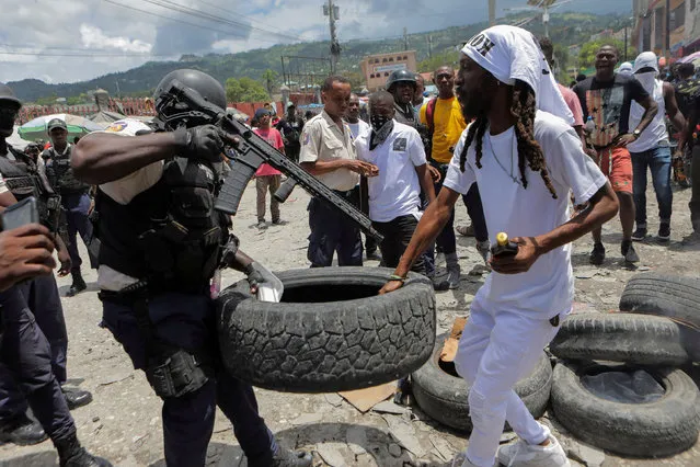 A police officer holding a gun confronts a demonstrator over setting a roadblock with a tire during a protest to demand justice for President Jovenel Moise a year after his assassination, in Port-au-Prince, Haiti on July 7, 2022. (Photo by Ralph Tedy Erol/Reuters)