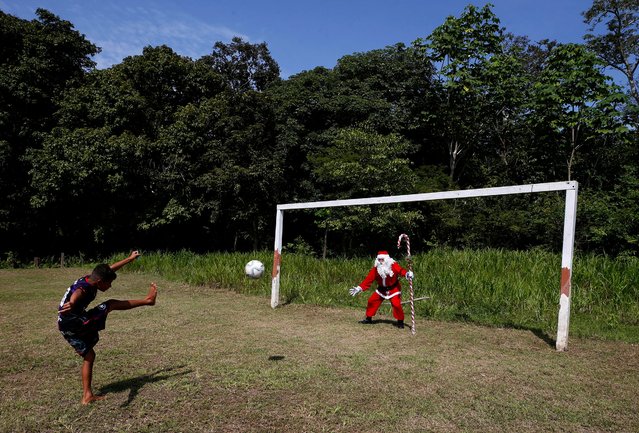 A young Amazonian resident strikes a ball towards Jorge Barroso, dressed as Santa Claus, who gave the ball to the boy after Barroso arrived on a boat to distribute Christmas gifts to children, in Iranduba, Brazil, Saturday, December 21, 2024. (Photo by Edmar Barros/AP Photo)