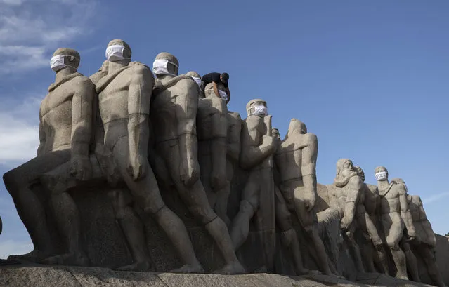 A city worker puts face masks on the “Monumento as Bandeiras”, a monument in honor of Brazil's colonizers by Italian-Brazilian sculptor Victor Brecheret, to promote mask wearing amid the new coronavirus pandemic in Sao Paulo, Brazil, Tuesday, May 12, 2020. (Photo by Andre Penner/AP Photo)