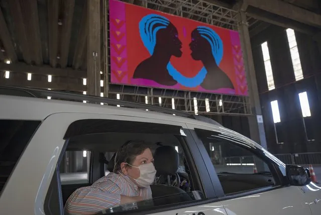 A woman takes in an art exhibit from the backseat of a car as she is driven through a warehouse displaying paintings and photos in Sao Paulo, Brazil, Friday, July 24, 2020, amid the new coronavirus pandemic. Galleries, cinemas, theaters and museums are closed due to the restrictive measures to avoid the spread of COVID-19, but a group of artists and a curator found a way to overcome the restrictions to share their art with the residents of Brazil’s largest city. (Photo by Andre Penner/AP Photo)