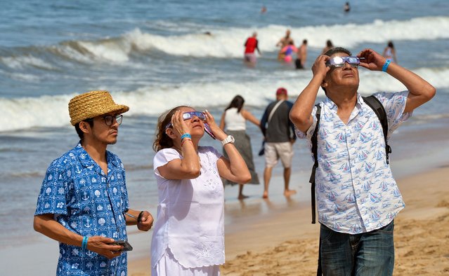 People look toward the sky as the moon begins to partially eclipse the sun at the beach in Mazatlan, Sinaloa State, Mexico, on April 8, 2024. This year's path of totality is 115 miles (185 kilometers) wide and home to nearly 32 million Americans, with an additional 150 million living less than 200 miles from the strip. The next total solar eclipse that can be seen from a large part of North America won't come around until 2044. (Photo by Mario Vazquez/AFP Photo)