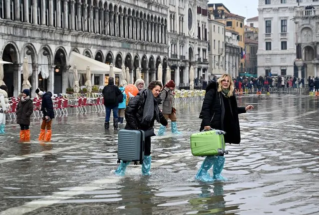 Tourists carry their luggage across a flooded St. Mark's square in Venice on December 10, 2022, following an “Alta Acqua” high tide event, too low to operate the MOSE Experimental Electromechanical Module that protects the city of Venice from floods. (Photo by Andrea Pattaro/AFP Photo)