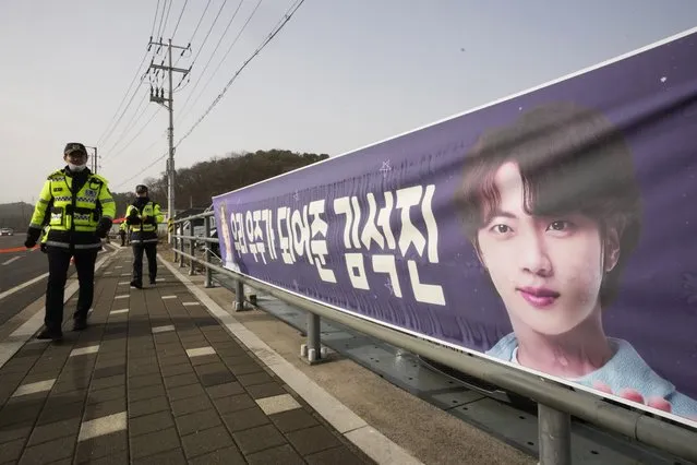 South Korean police officers pass by a banner showing an image of K-pop band BTS's member Jin near an army training center in Yeoncheon, South Korea, Tuesday, December 13, 2022. Jin is set to enter a frontline South Korean booth camp on Tuesday to start his 18 months of mandatory military service, as fans are gathering near the base to say goodbye to their star. (Photo by Ahn Young-joon/AP Photo)