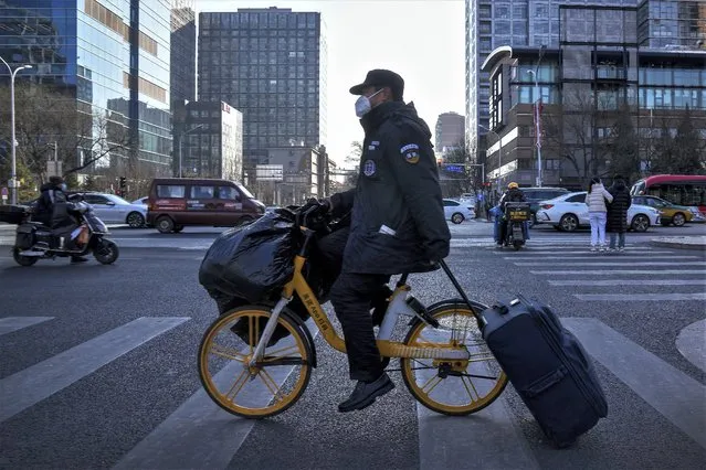 A security guard wearing a face mask and using a bike-sharing service carries his belonging rides across a street in Beijing, Monday, January 9, 2023. China's healthcare authorities declined to include Pfizer's COVID-treatment drug in a national reimbursement list that would've allowed patients to get it at a cheaper price throughout the country, saying it was too expensive. (Photo by Andy Wong/AP Photo)