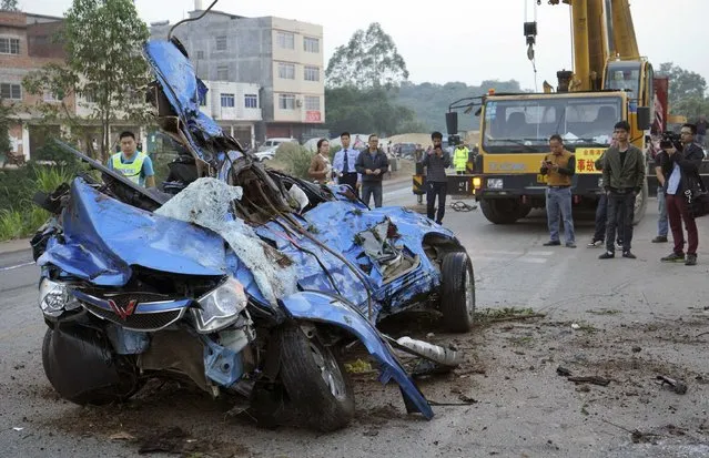People look at a destroyed minivan after it collided with a truck and fell off a ramp on the side of a street, in Nanning, Guangxi Zhuang Autonomous Region November 22, 2014. (Photo by Reuters/Stringer)
