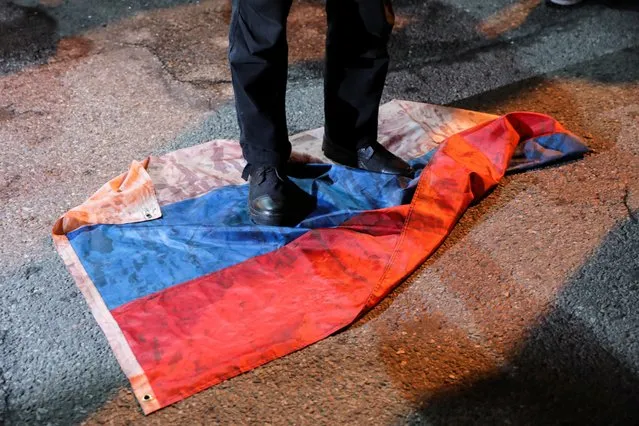 A person stands on a Russian flag during a candlelight vigil in front of the Russian embassy on the one year anniversary of the Russian invasion of Ukraine, in New York City, New York on February 23, 2023. (Photo by Irynka Hromotska/Reuters)