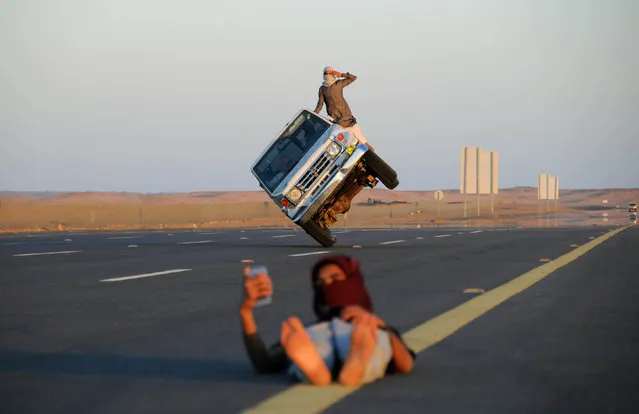 Saudi men perform a stunt known as “sidewall skiing” (driving on two wheels) as a youth takes a selfie in Tabuk, Saudi Arabia March 11, 2018. (Photo by Mohamed Al Hwaity/Reuters)