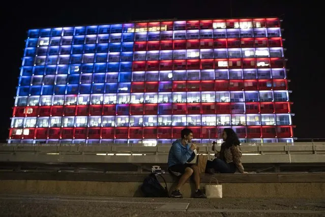 An Israeli couple sits near the Tel Aviv municipality building as it is lit up with the flag of the United States in Tel Aviv, Israel, Thursday, January 7, 2021. Officials said the display is a sign of solidarity with the United States and support for democracy. (Photo by Sebastian Scheiner/AP Photo)