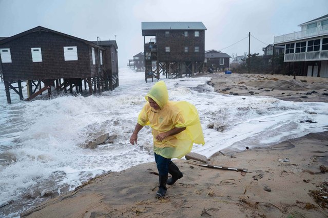 A man walks past houses at risk of collapse during a storm in Buxton, North Carolina, on Sunday, October 12, 2025. Coastal flooding and wind-whipped rain hit the mid-Atlantic and Northeast coastline as an impactful nor’easter crawled up the East Coast. (Photo by Allison Joyce/AP Photo)